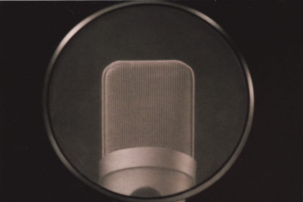 A broadcast microphone behind a round pop filter, lit along its grille.