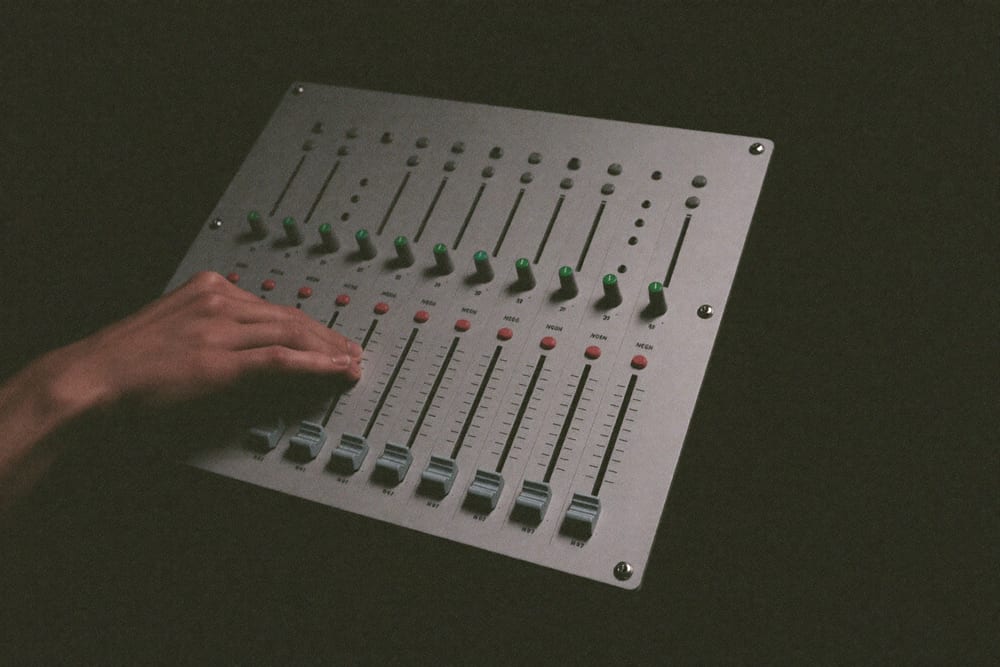 A hand on the faders of a small mixing desk in a dark control room.