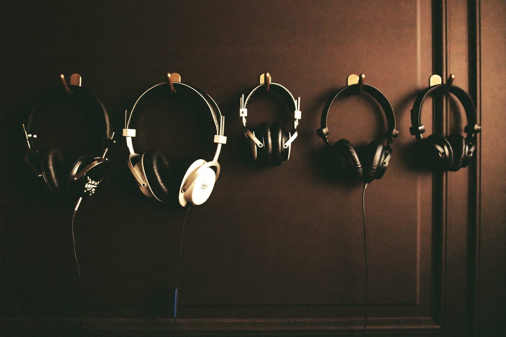 Four pairs of studio headphones hanging on brass hooks against a dark panelled wall.