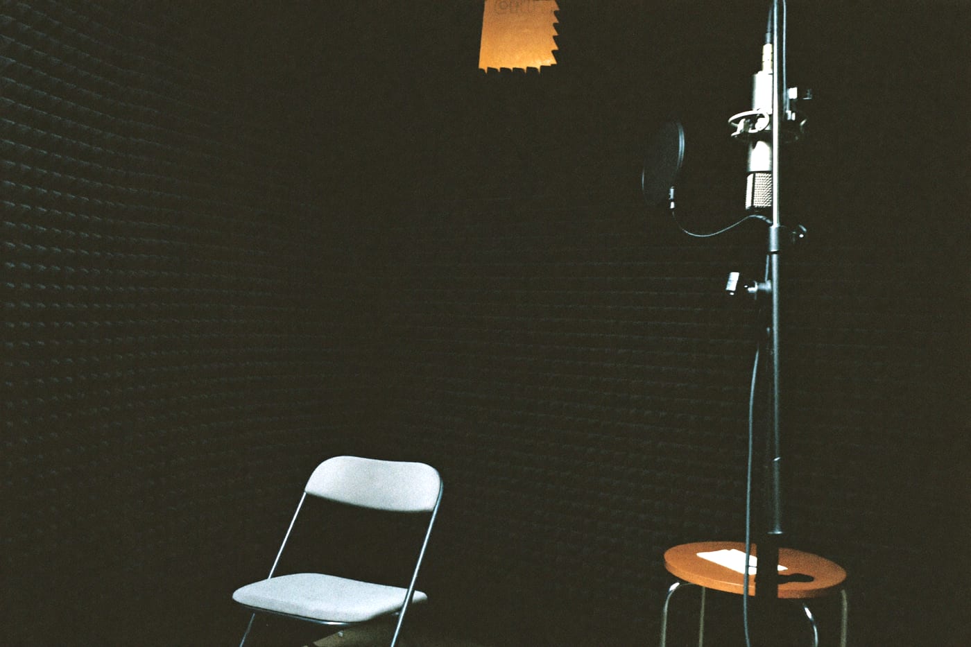 A small single-person recording booth with one microphone, one chair and thick acoustic padding.